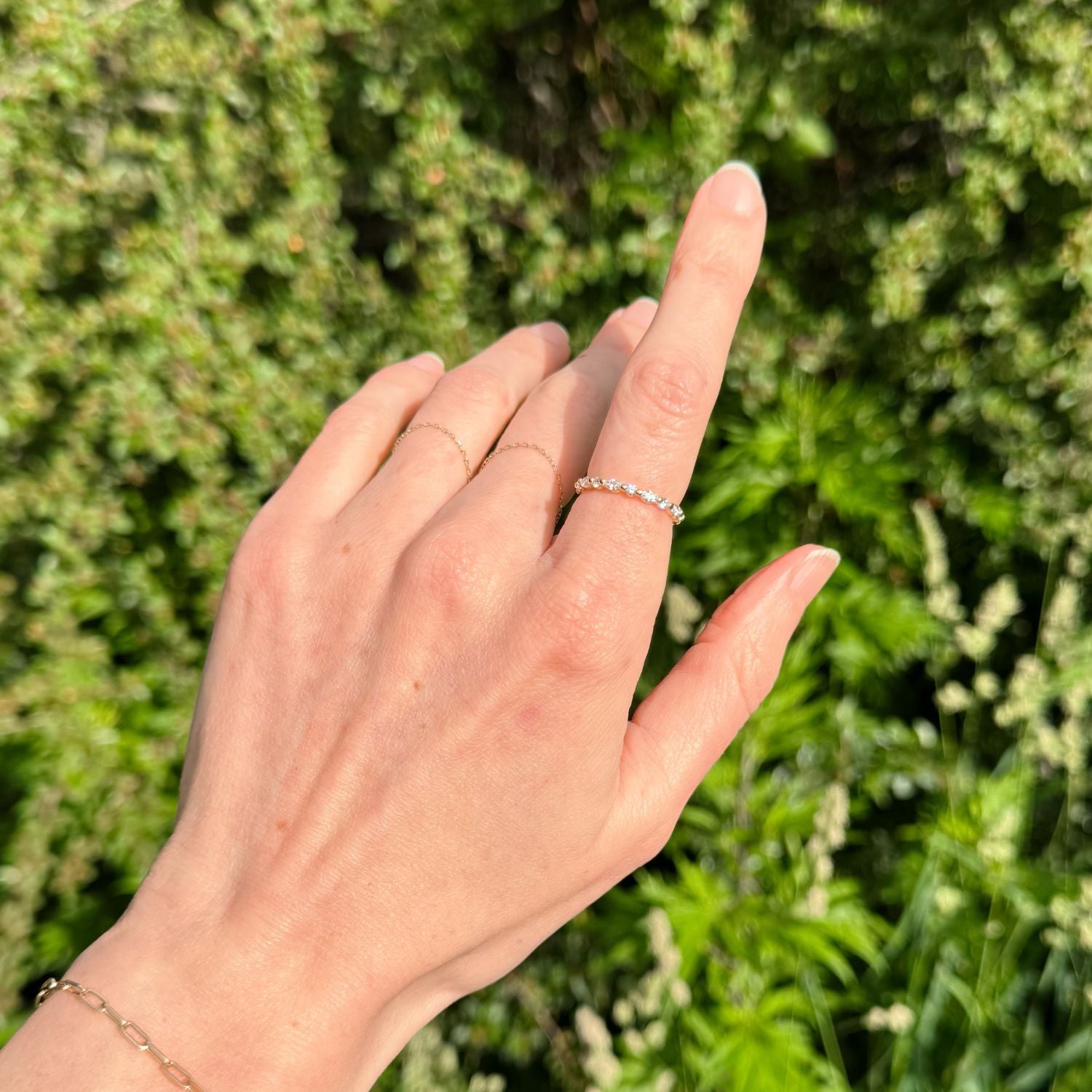 Hand wearing an eternity diamond ring with a green leaf background