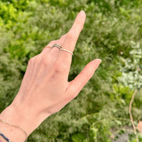 Hand with an eternity diamond ring pointing upwards against a green blurred background