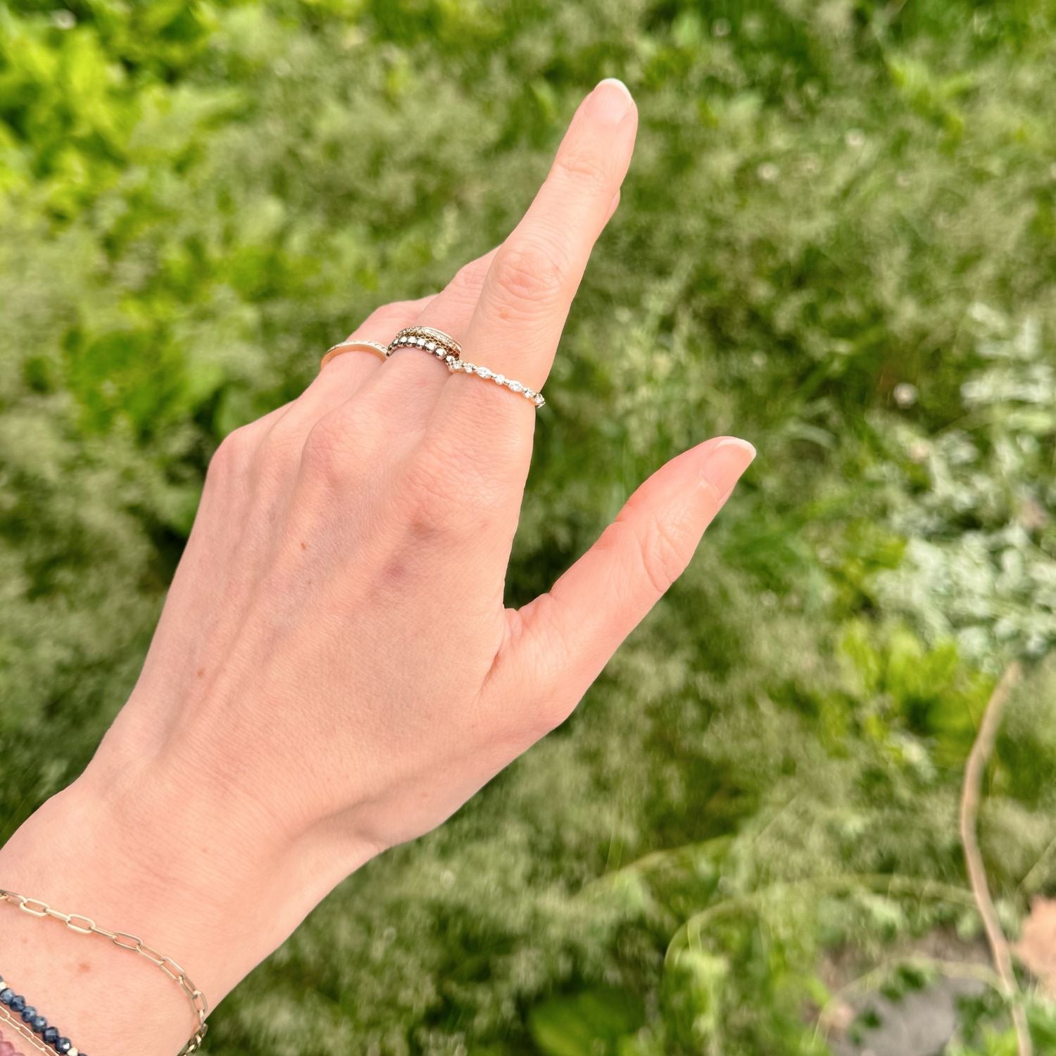 Hand with an eternity diamond ring pointing upwards against a green blurred background