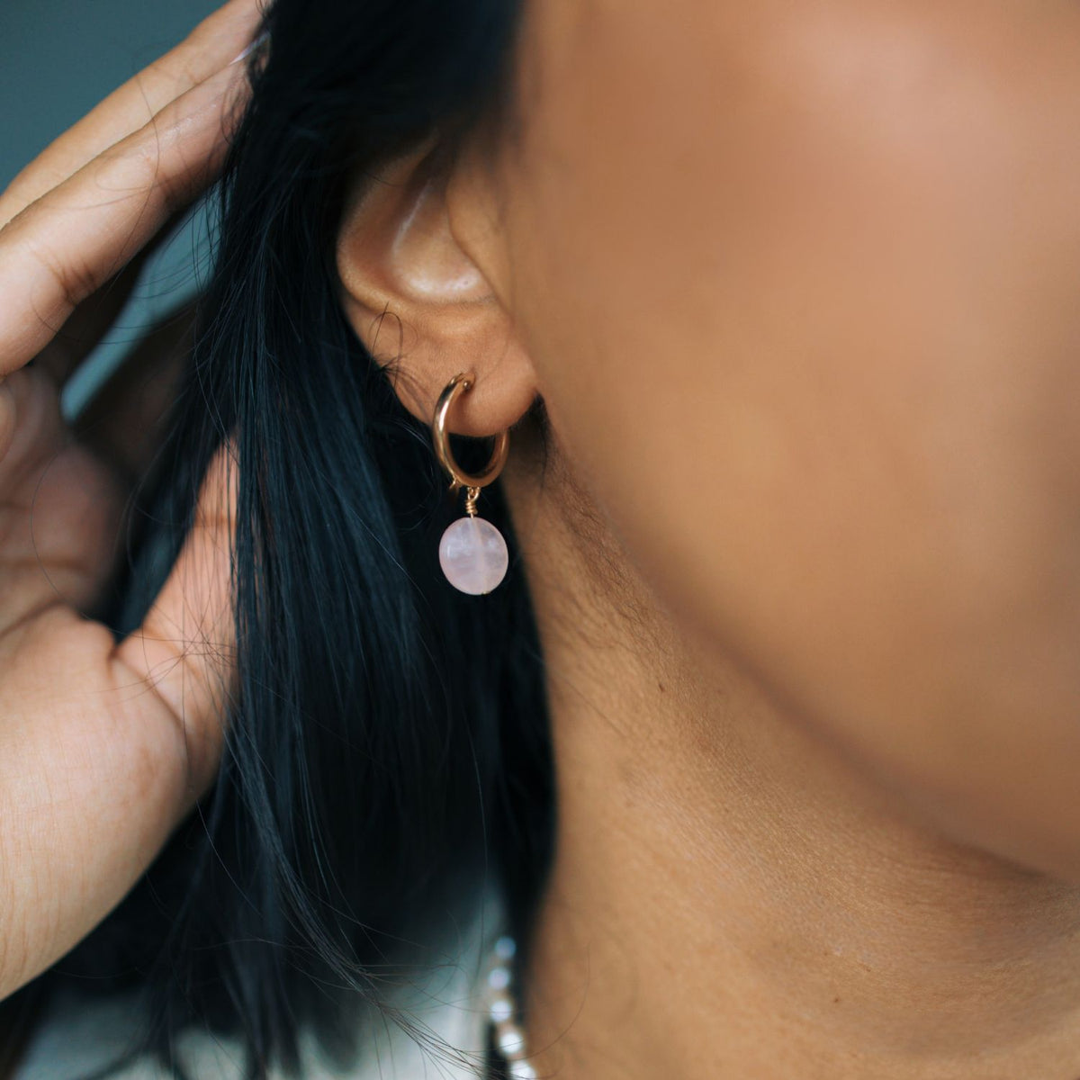 Close-up of an ear wearing a gold hoop earring with a pink gemstone, with hair partially covering the face.