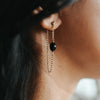 Close-up of an ear wearing a gold chain earring with a black bead.