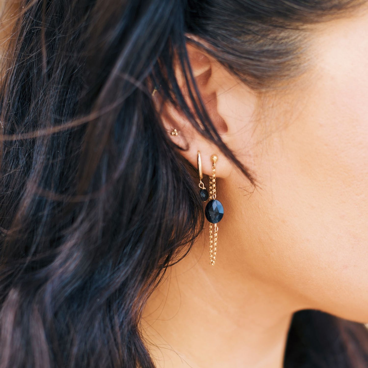 Close-up of a person wearing gold chain loop earrings with black onyx stone.