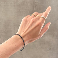 Hand wearing a blue sapphire bead bracelet and multiple rings on a neutral background