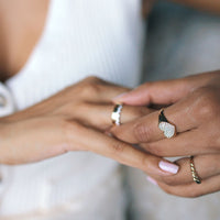 Close-up of hands with multiple solid gold and diamond stacking rings on a blurred background