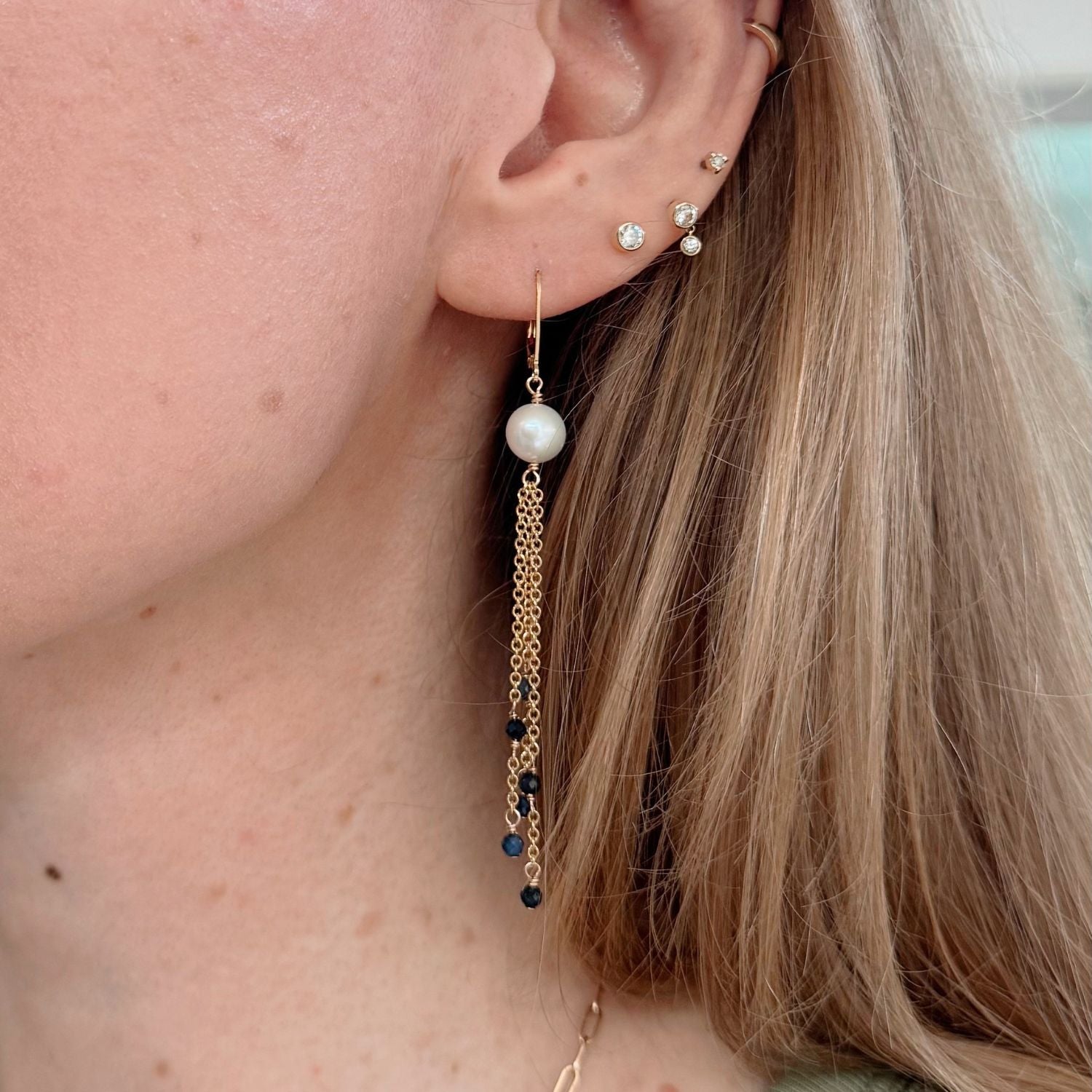 Close-up of an ear with pearl and gold chain earrings with blue sapphires.