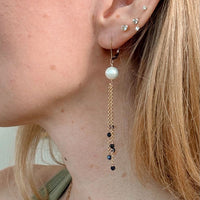 Close-up of an ear wearing a pearl and chain earring with blue sapphires on a neutral background