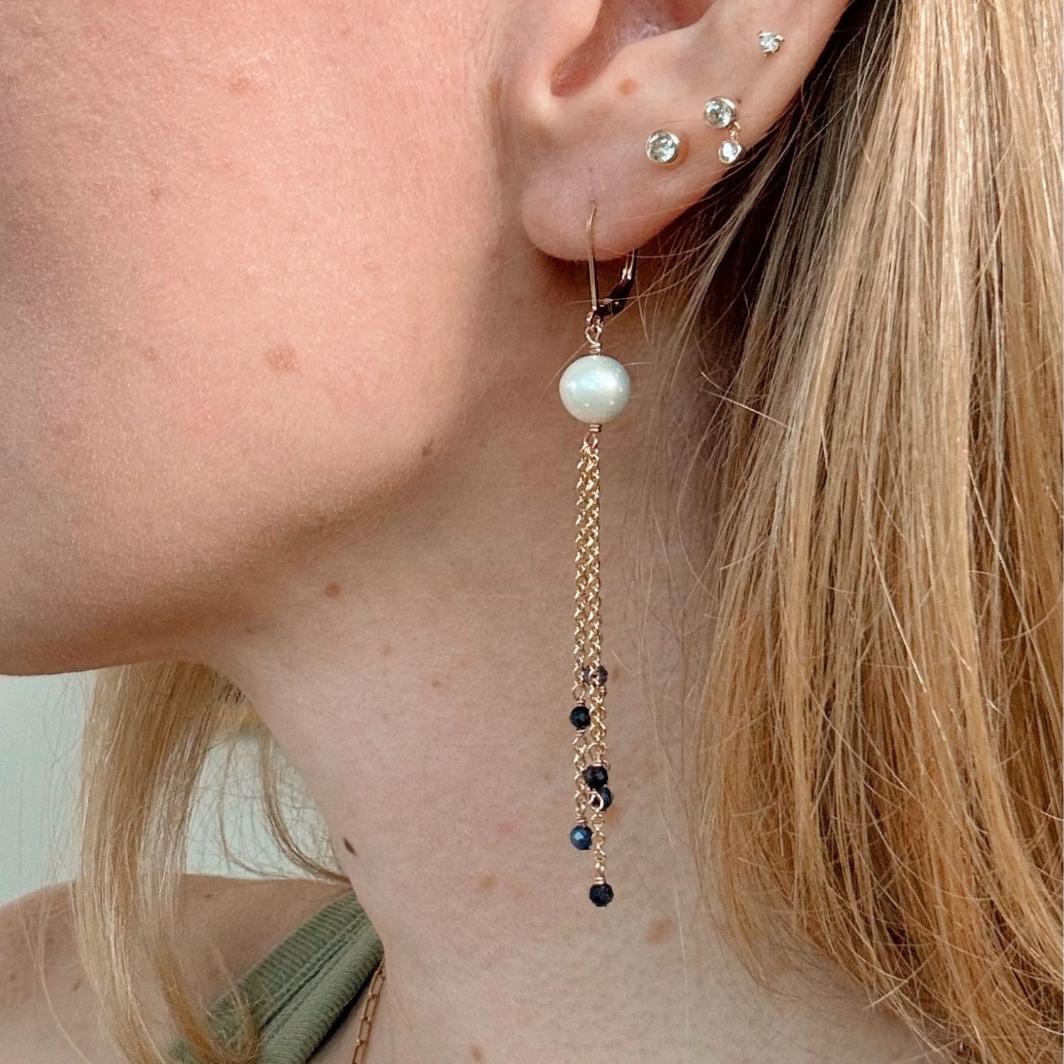 Close-up of an ear wearing a pearl and chain earring with blue sapphires on a neutral background