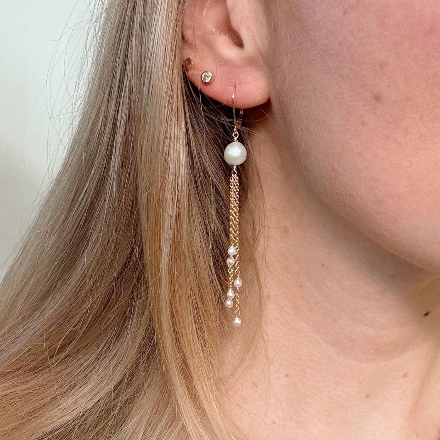 close up of ear wearing gold chain earrings with pearls