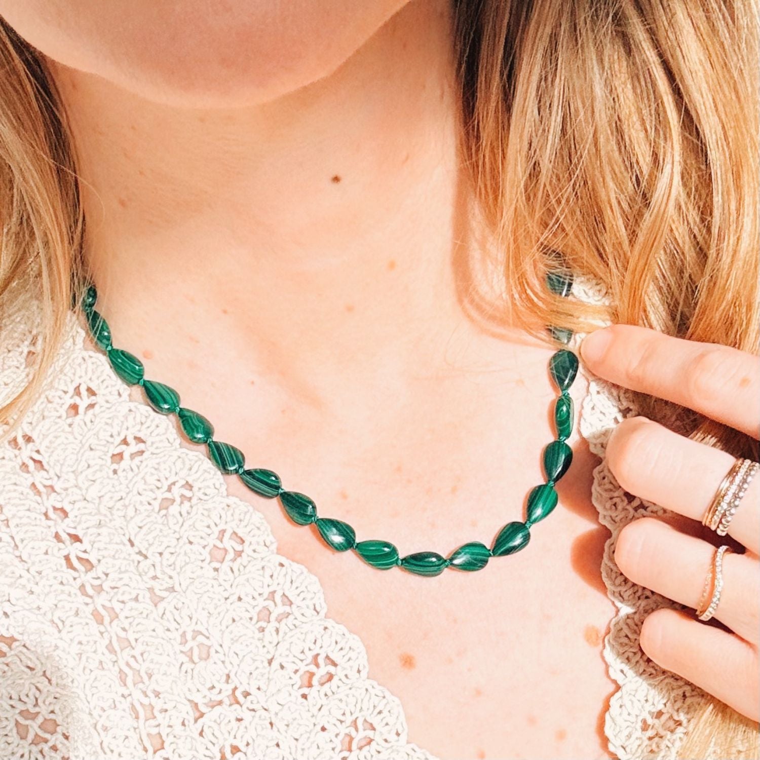 Natural malachite beaded necklace being held by a person with blonde hair.
