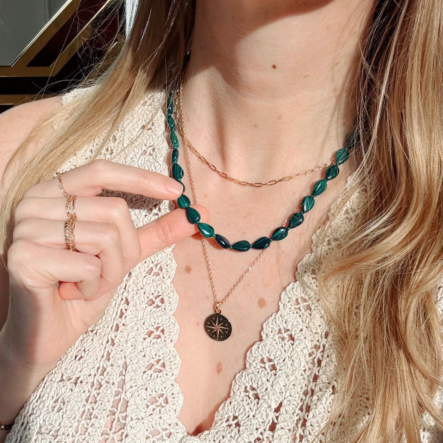 Person wearing multiple necklaces with a focus on green beaded necklace and gold chain.