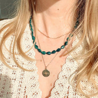Close-up of a person wearing layered necklaces with green beads and a gold chain.