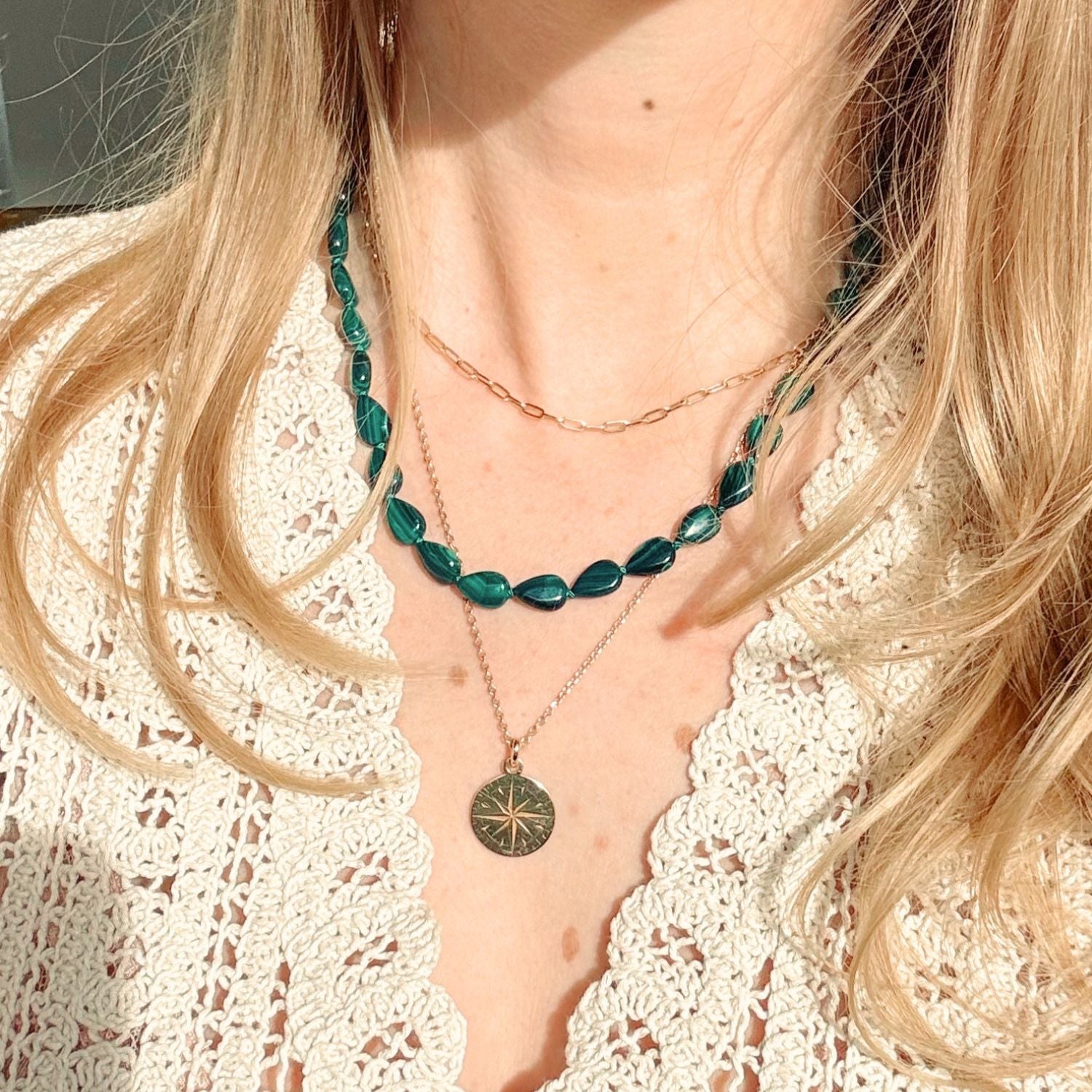 Close-up of a person wearing layered necklaces with green beads and a gold chain.