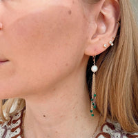 Close-up of a woman wearing gold chain pearl earrings with a blurred background