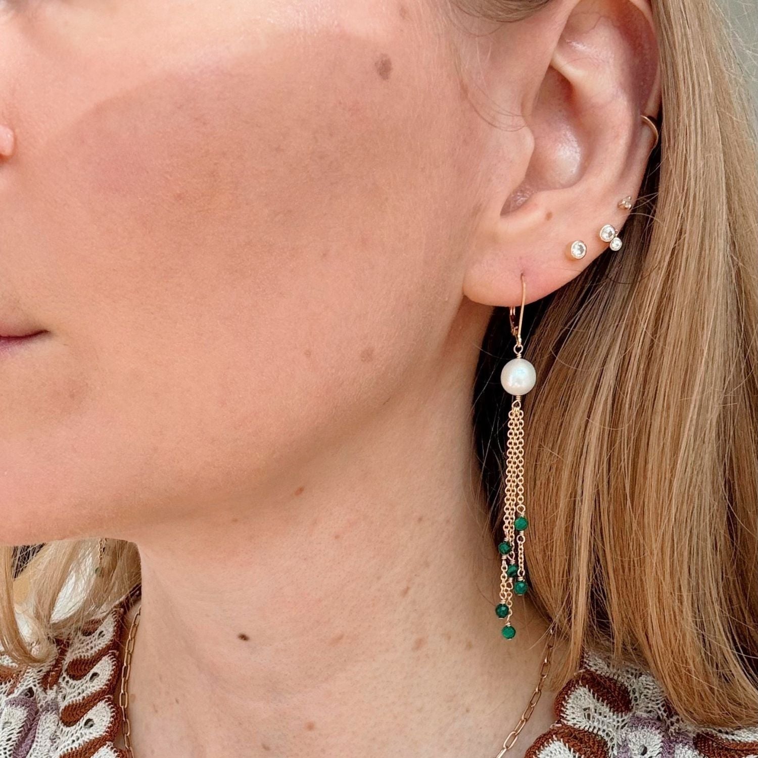 Close-up of a woman wearing gold chain pearl earrings with a blurred background