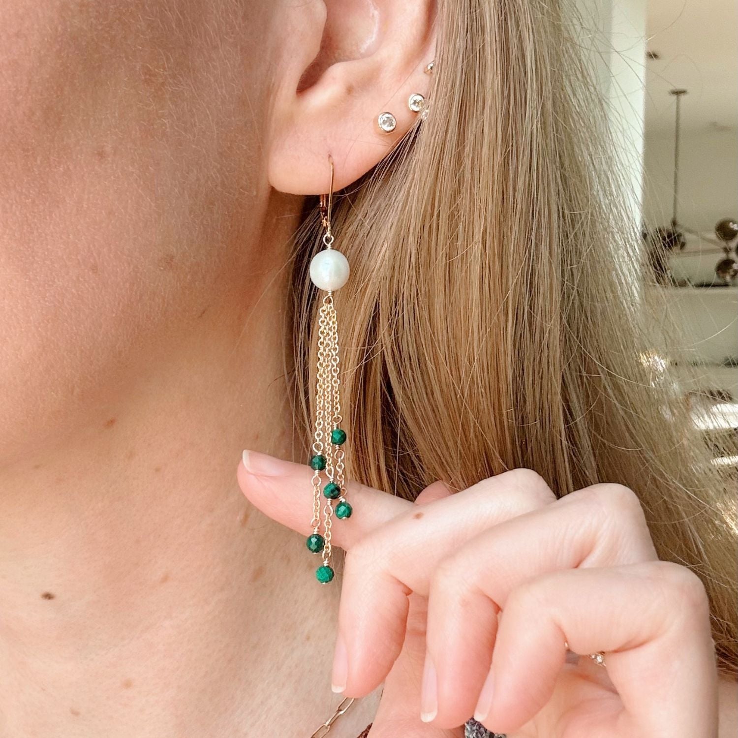 Close-up of a person wearing chain pearl and green bead earrings.