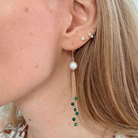 Close-up of a person wearing pearl and green bead earrings.