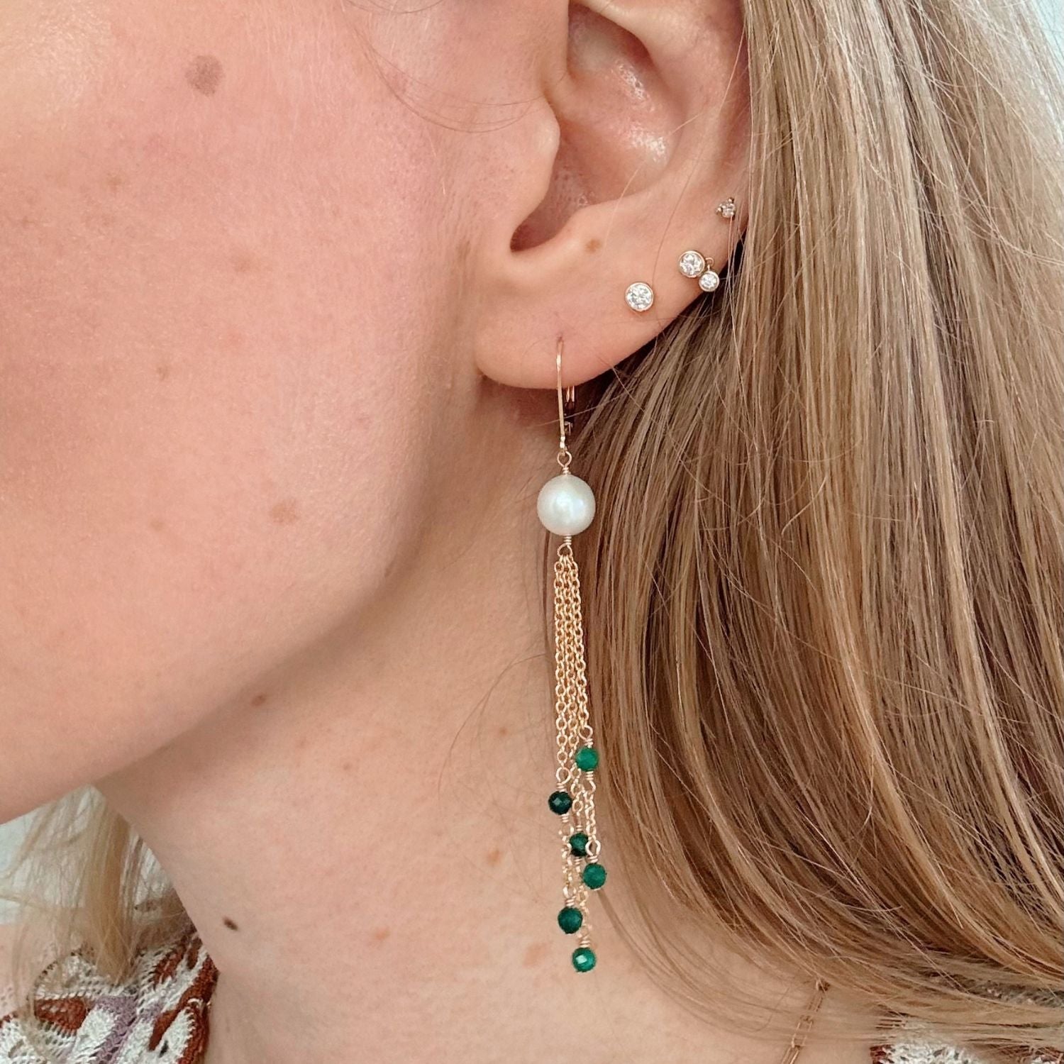 Close-up of a person wearing pearl and green bead earrings.