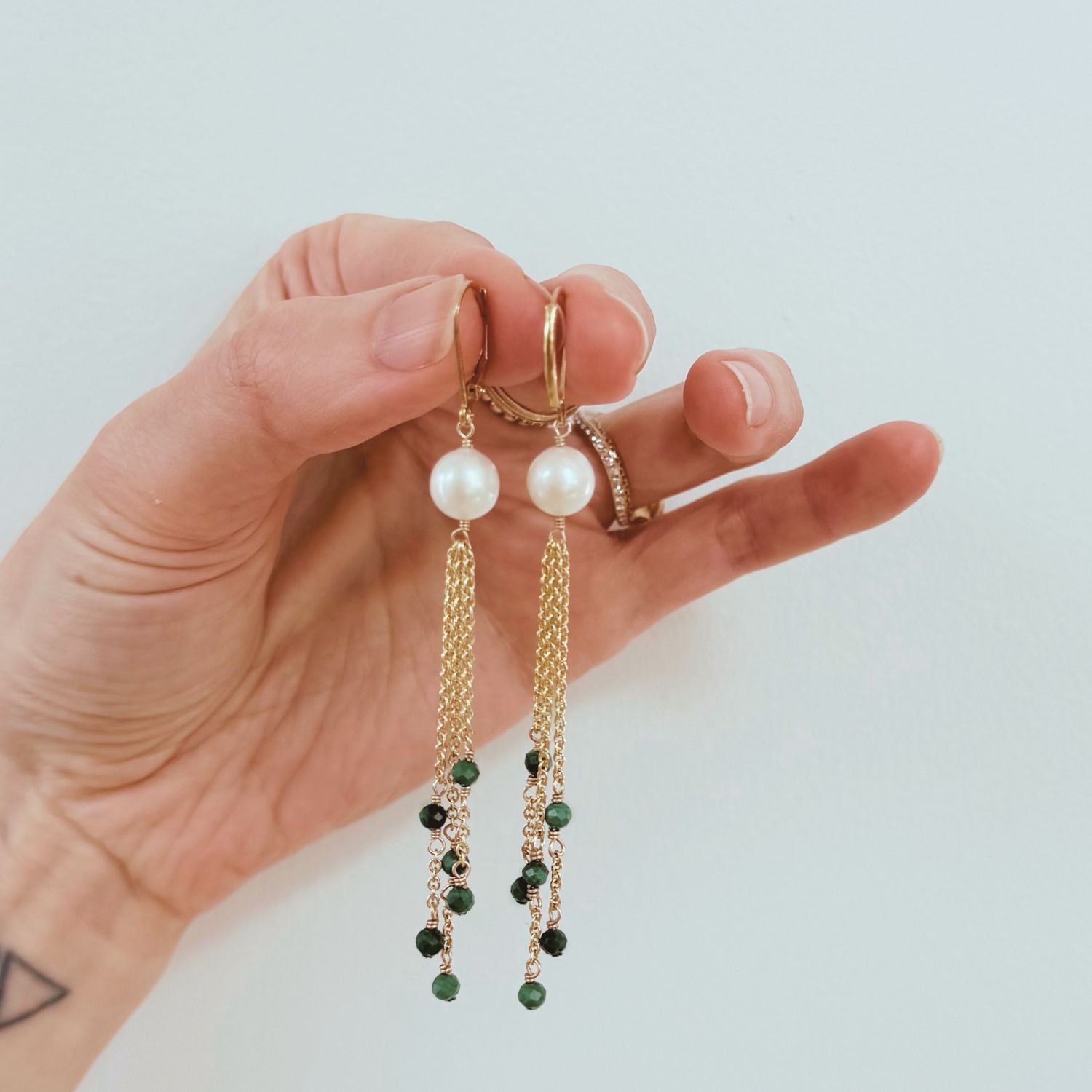 Hand holding a pair of pearl and green bead earrings against a light background