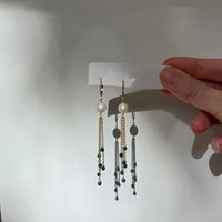 Pair of earrings on a white card held by a hand against a neutral background