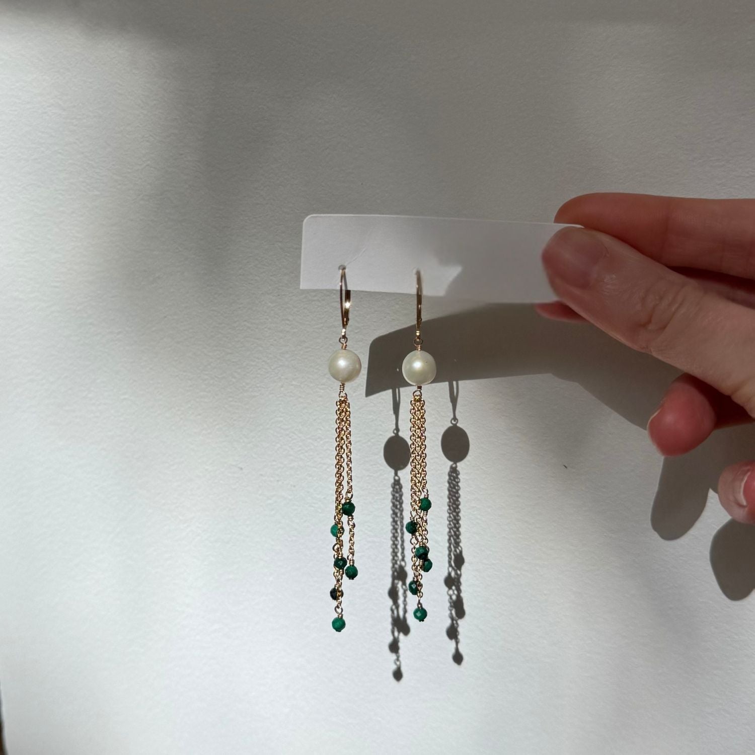 Pair of earrings on a white card held by a hand against a neutral background