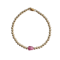Gold bracelet with a pink gemstone on a white background