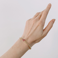 Hand wearing a gold bracelet with a pink stone on a plain background