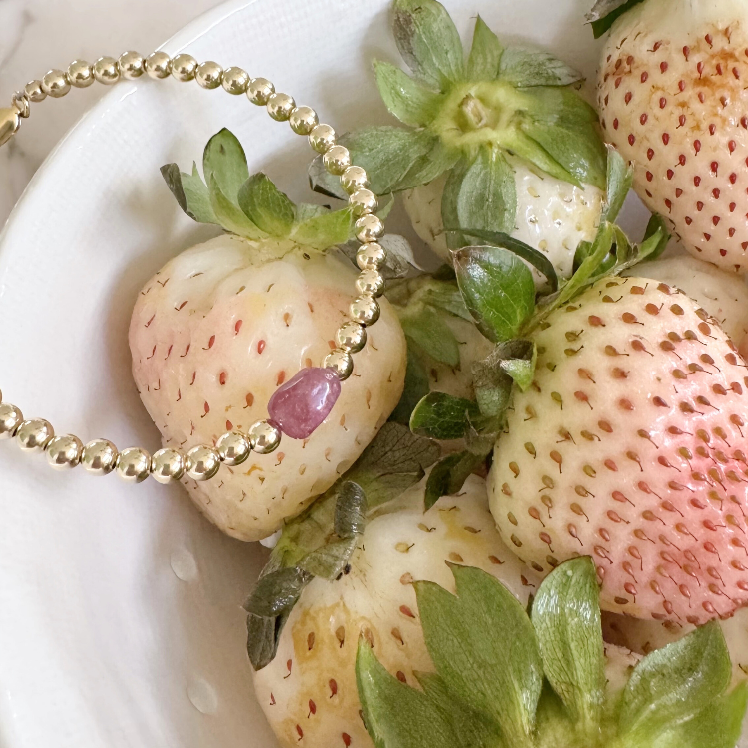 Gold beaded bracelet with a pink gemstone on strawberries