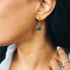 Close-up of a person wearing a gold earring with a green gemstone.