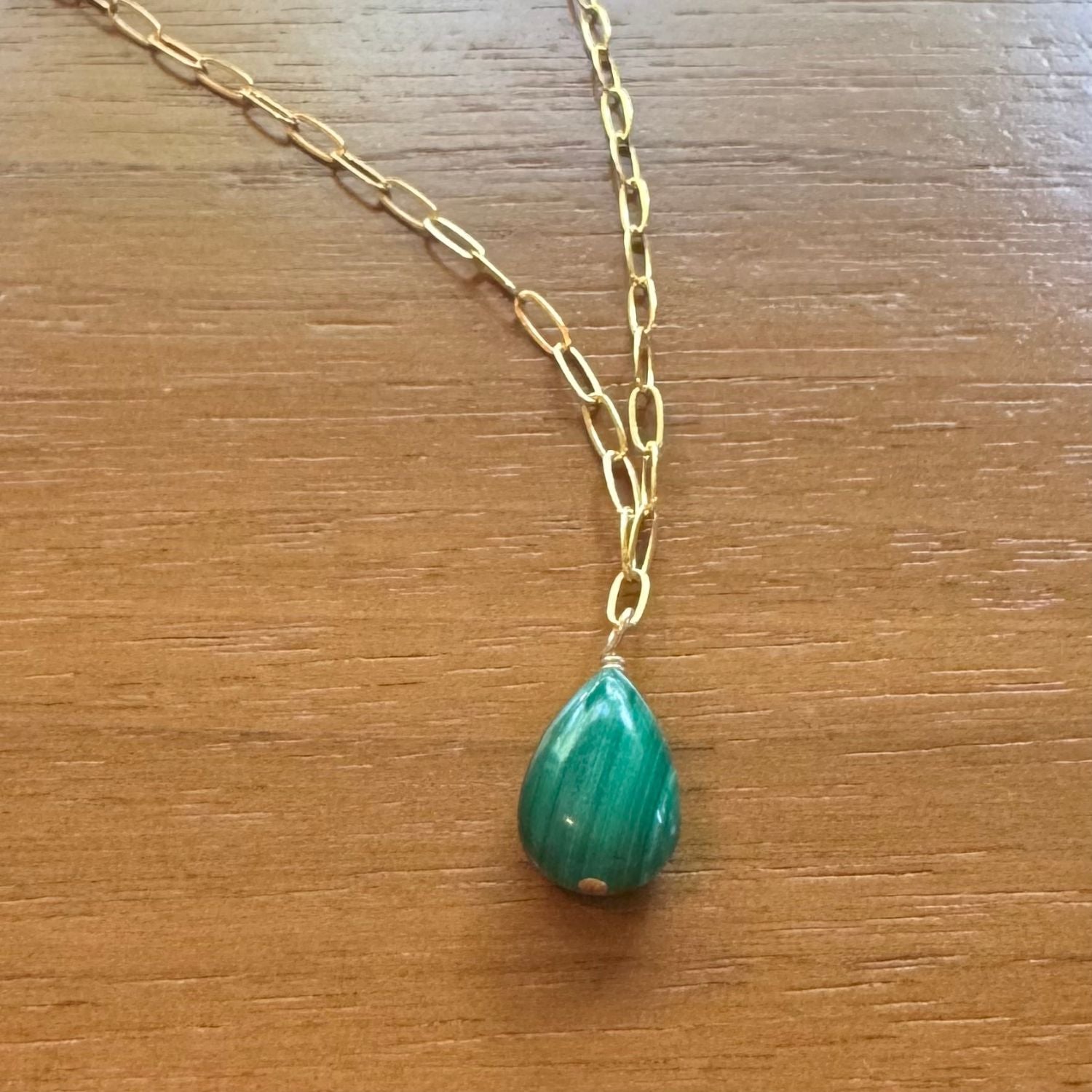 Gold necklace with a green malachite teardrop pendant on a wooden surface