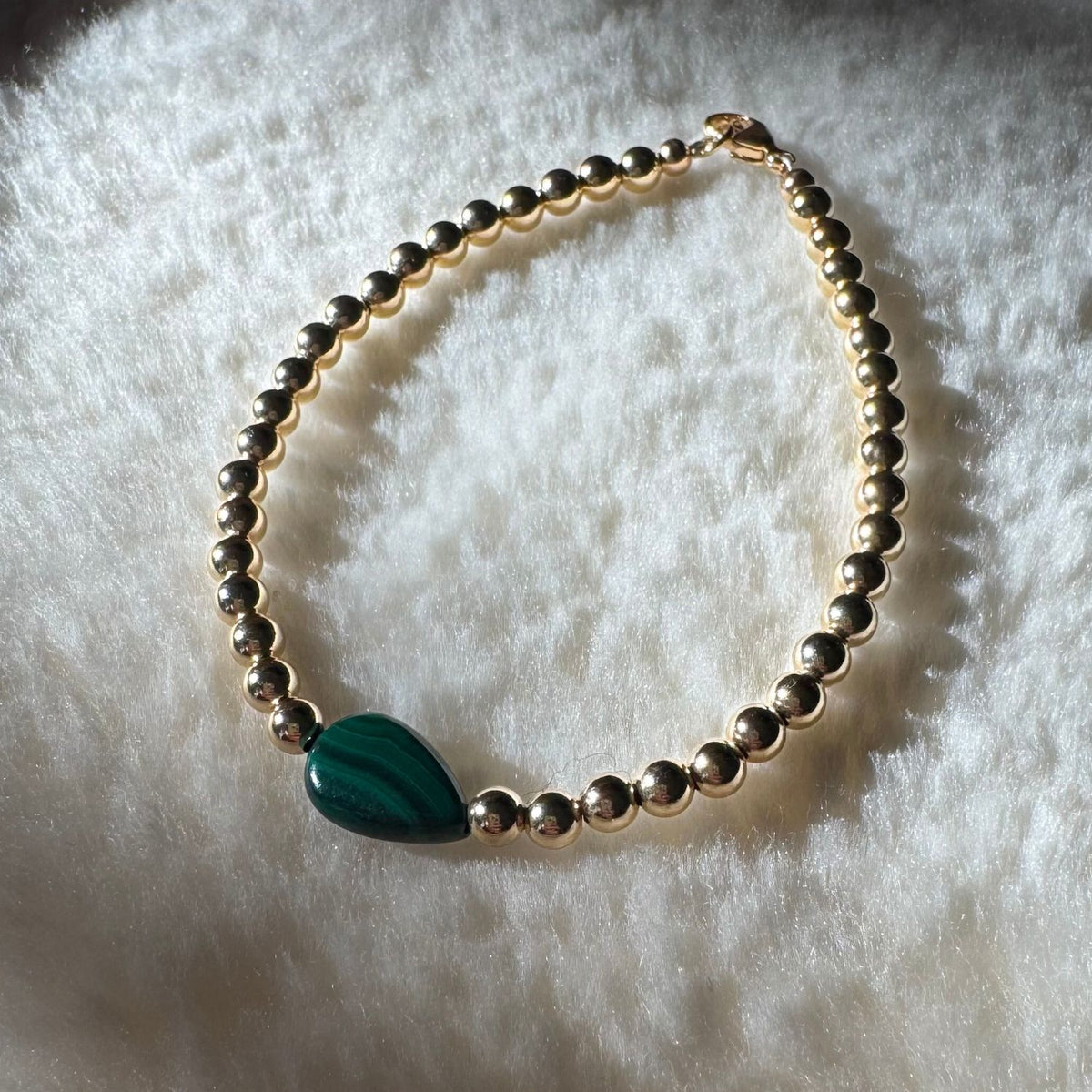 Gold Filled Bead Bracelet with a teardrop shaped malachite stone in the center set on a cream background