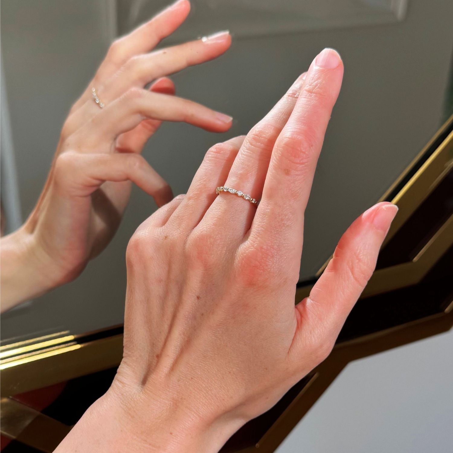 Close-up of a hand wearing a diamond ring with a mirror reflection background