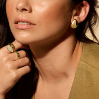 Close-up of a woman wearing 14k yellow gold earrings and rings, with a neutral background.