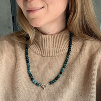 Woman wearing a bold green necklace with a toggle clasp over a tan sweater. 