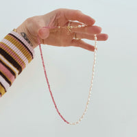 Hand holding a pink and pearl beaded necklace with a plain background