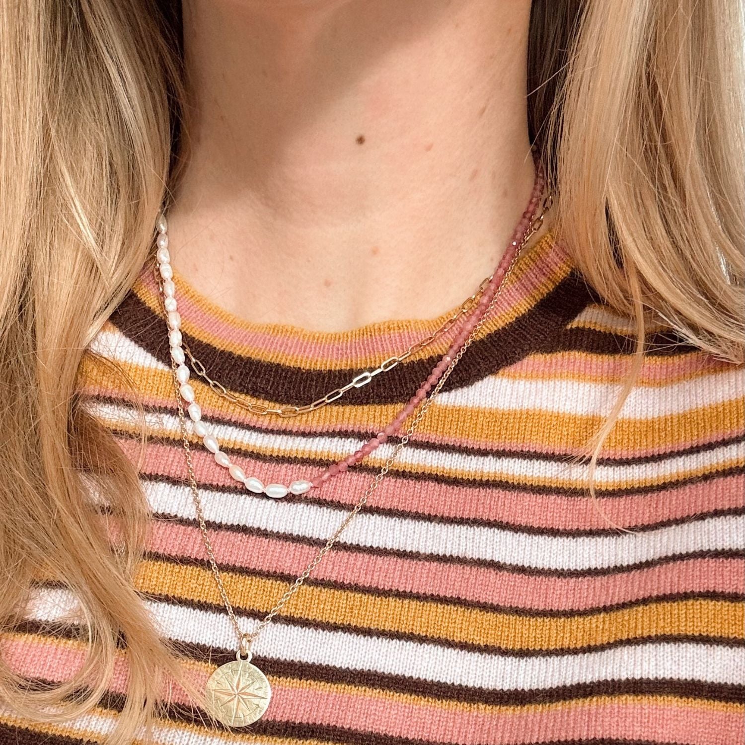 Close-up of a person wearing a striped shirt with layered necklaces.