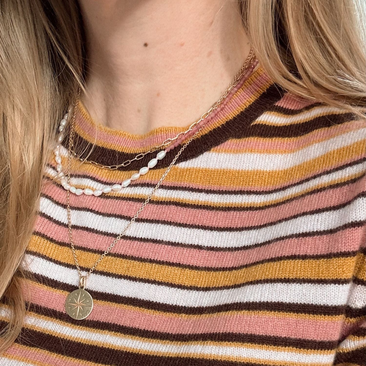 Close-up of a person wearing a striped shirt with layered necklaces.