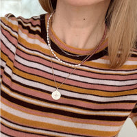 Person wearing a striped sweater with a necklace featuring a circular pendant.