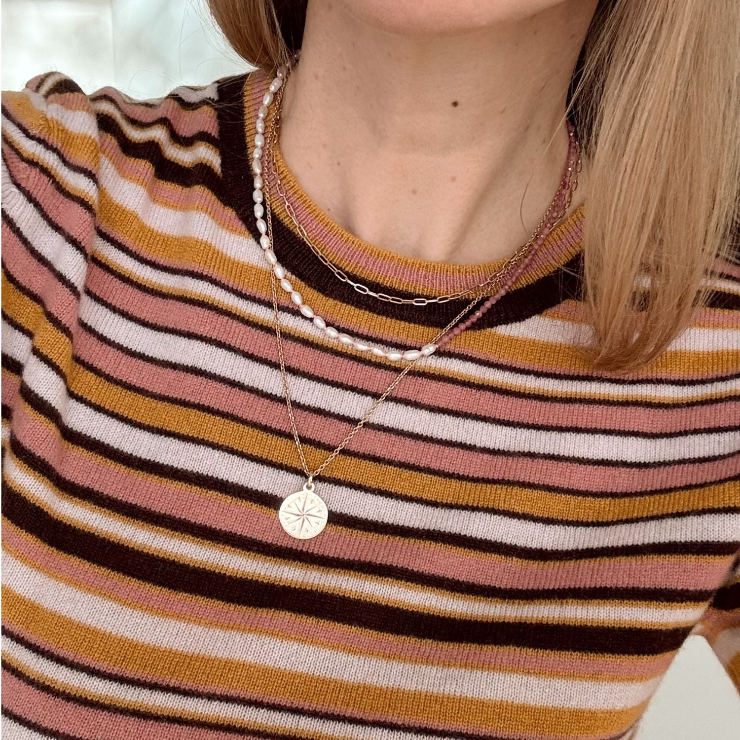 Person wearing a striped sweater with a necklace featuring a circular pendant.