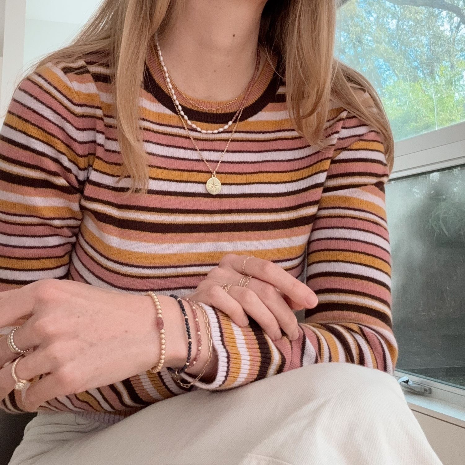 Person wearing a striped sweater with jewelry, sitting indoors.