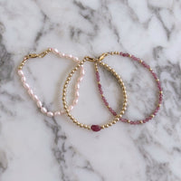 Two pink tourmaline and gold beaded bracelets and one pink pearl bracelet on a marble background