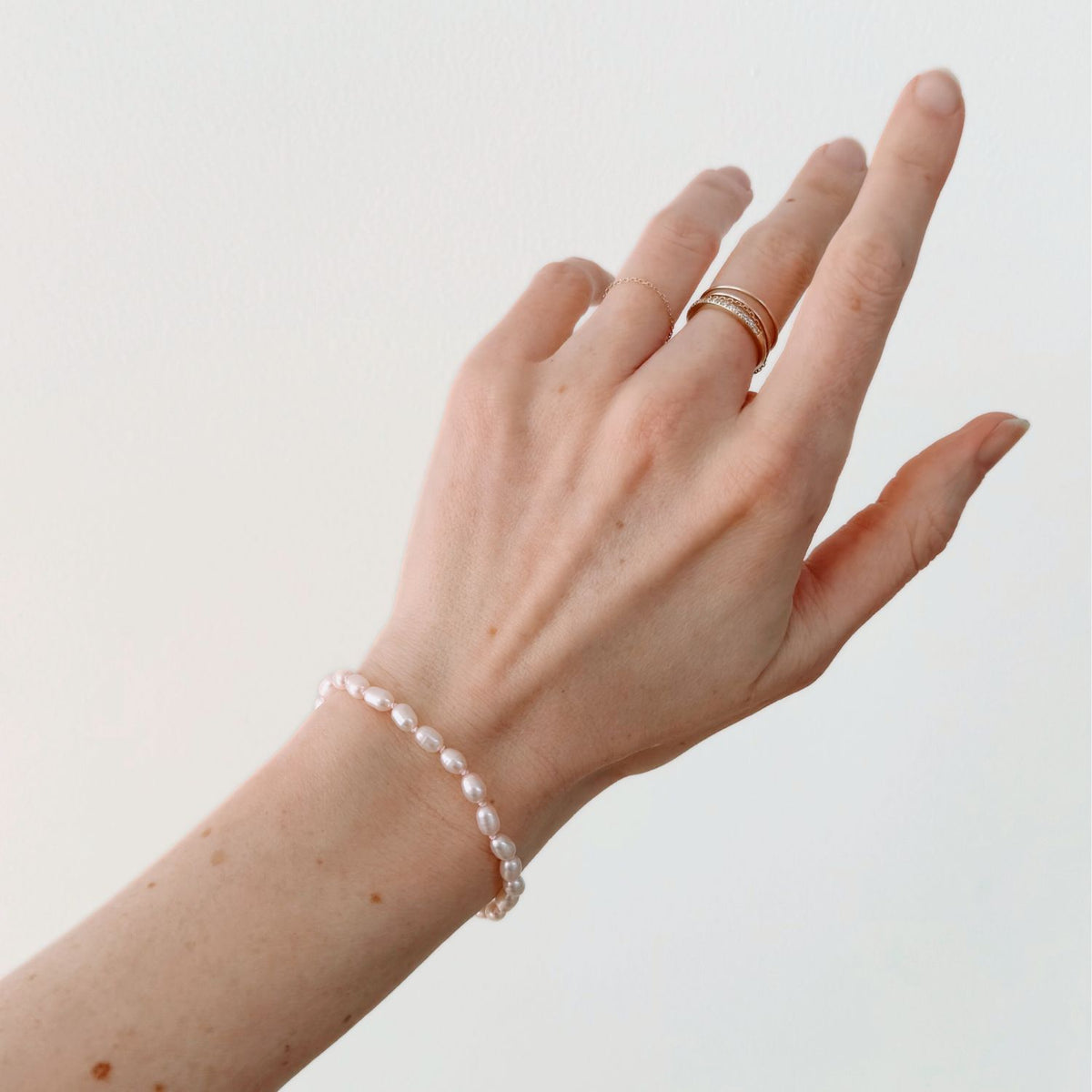 Hand wearing a freshwater pink pearl bracelet and gold ring on a plain background