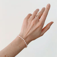 Hand wearing a freshwater pink pearl bracelet and gold ring on a plain background