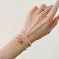 Hand wearing a gold beaded bracelet and a freshwater pink pearl bracelet on a neutral background