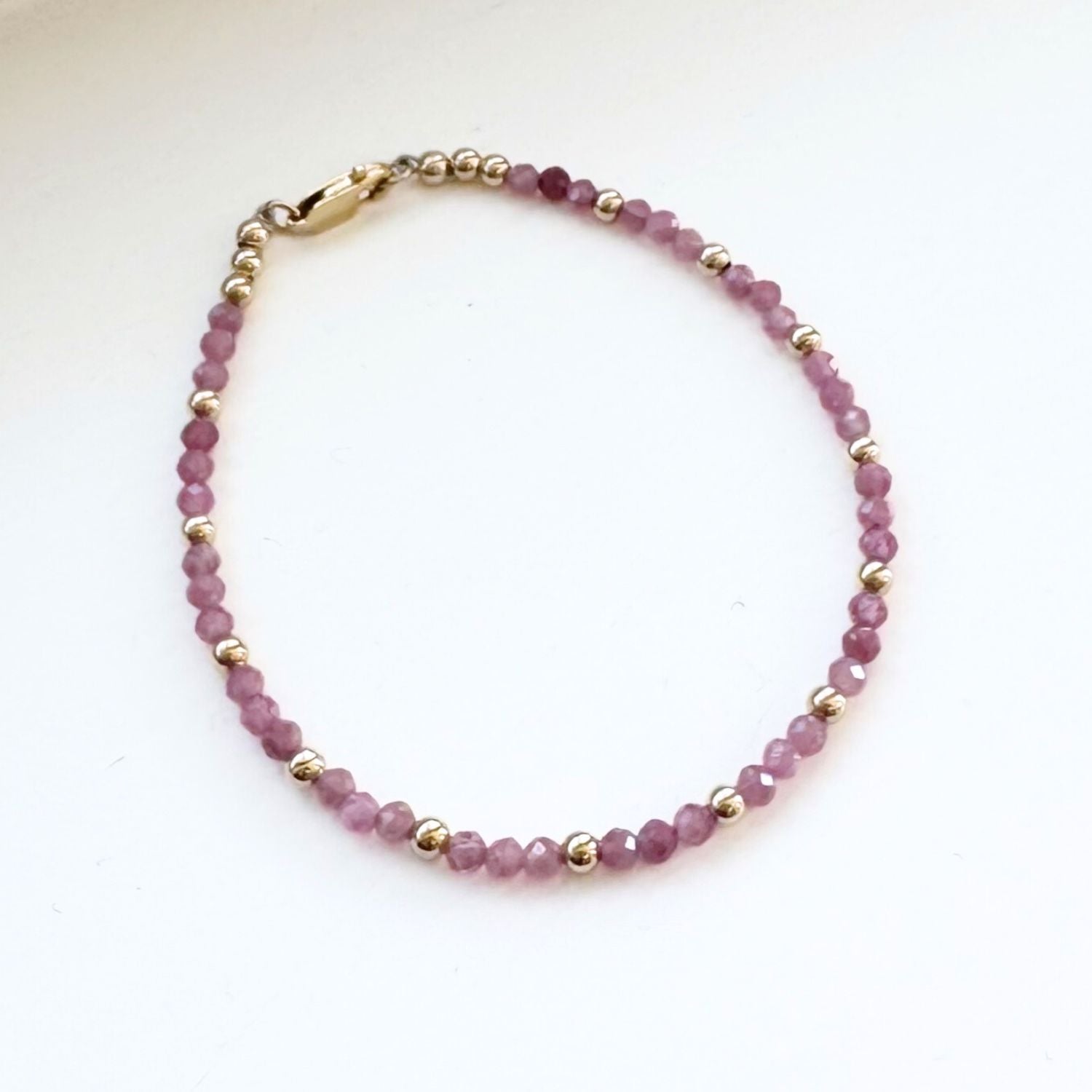 Beaded bracelet with pink beads and gold accents on a white background