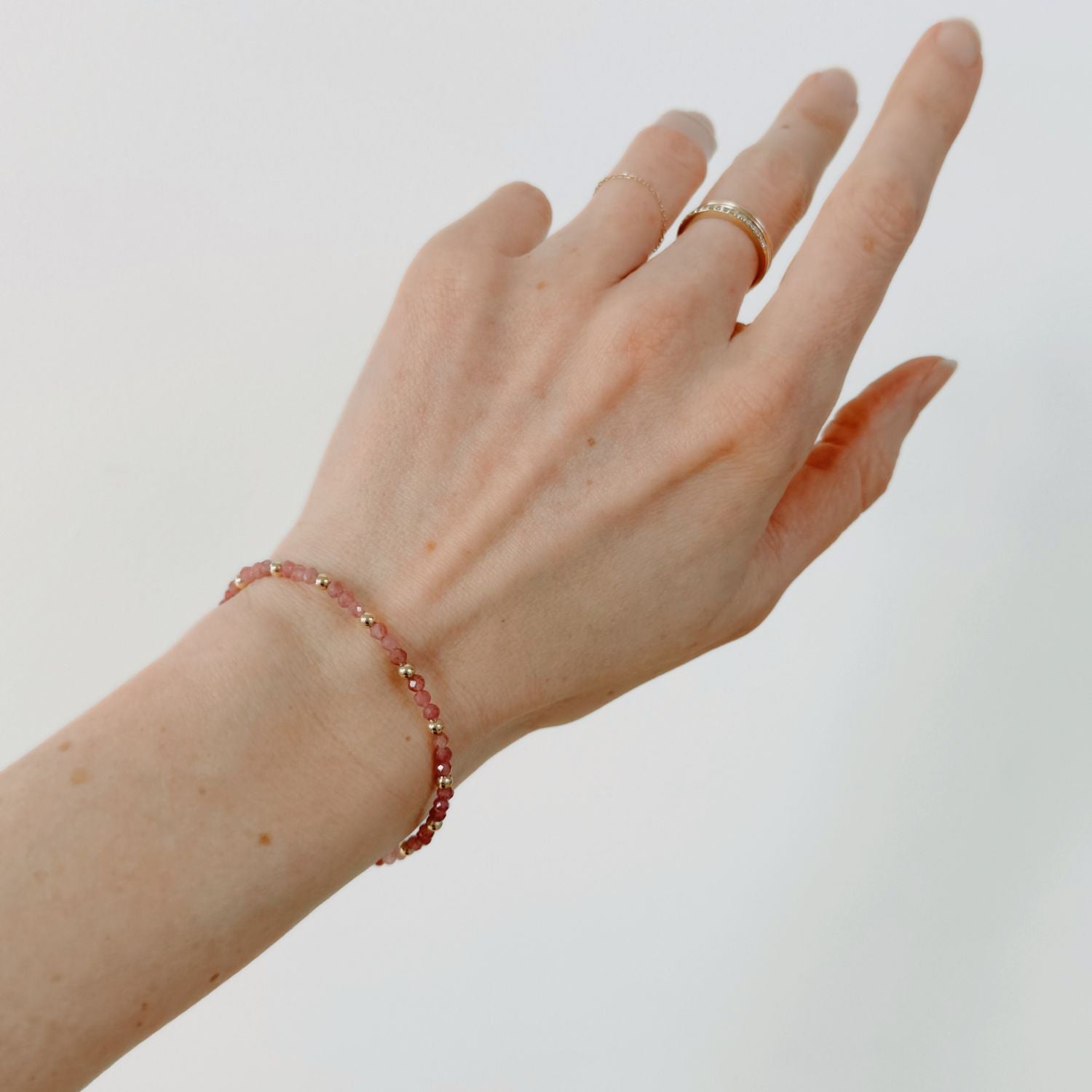Hand wearing a pink tourmaline bracelet and ring on a plain background