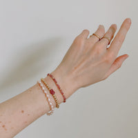 Hand wearing multiple pink and gold bracelets and rings on a plain background