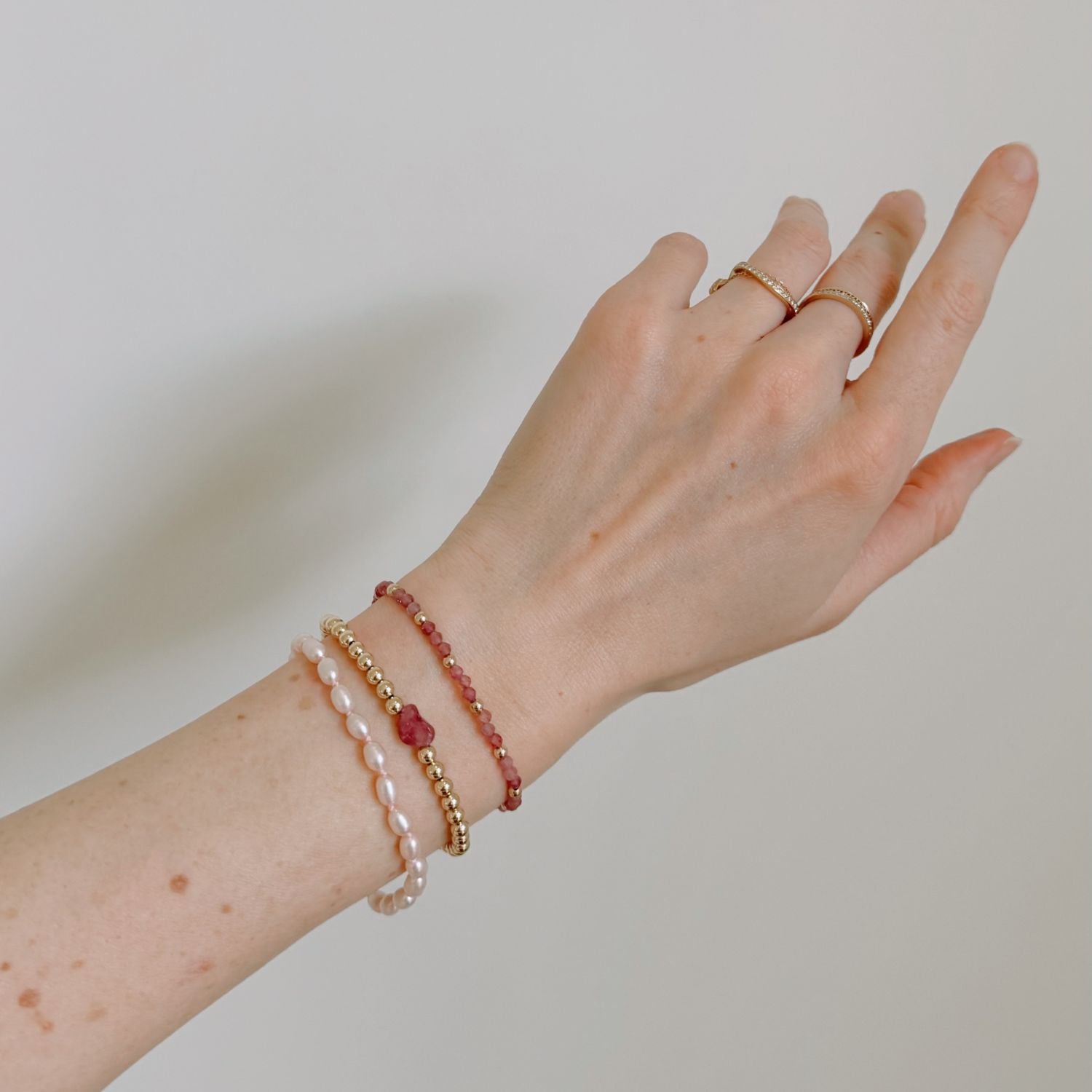 Hand wearing multiple pink and gold bracelets and rings on a plain background