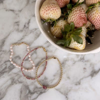 Three pink beaded bracelets on a marble surface with a bowl of strawberries.