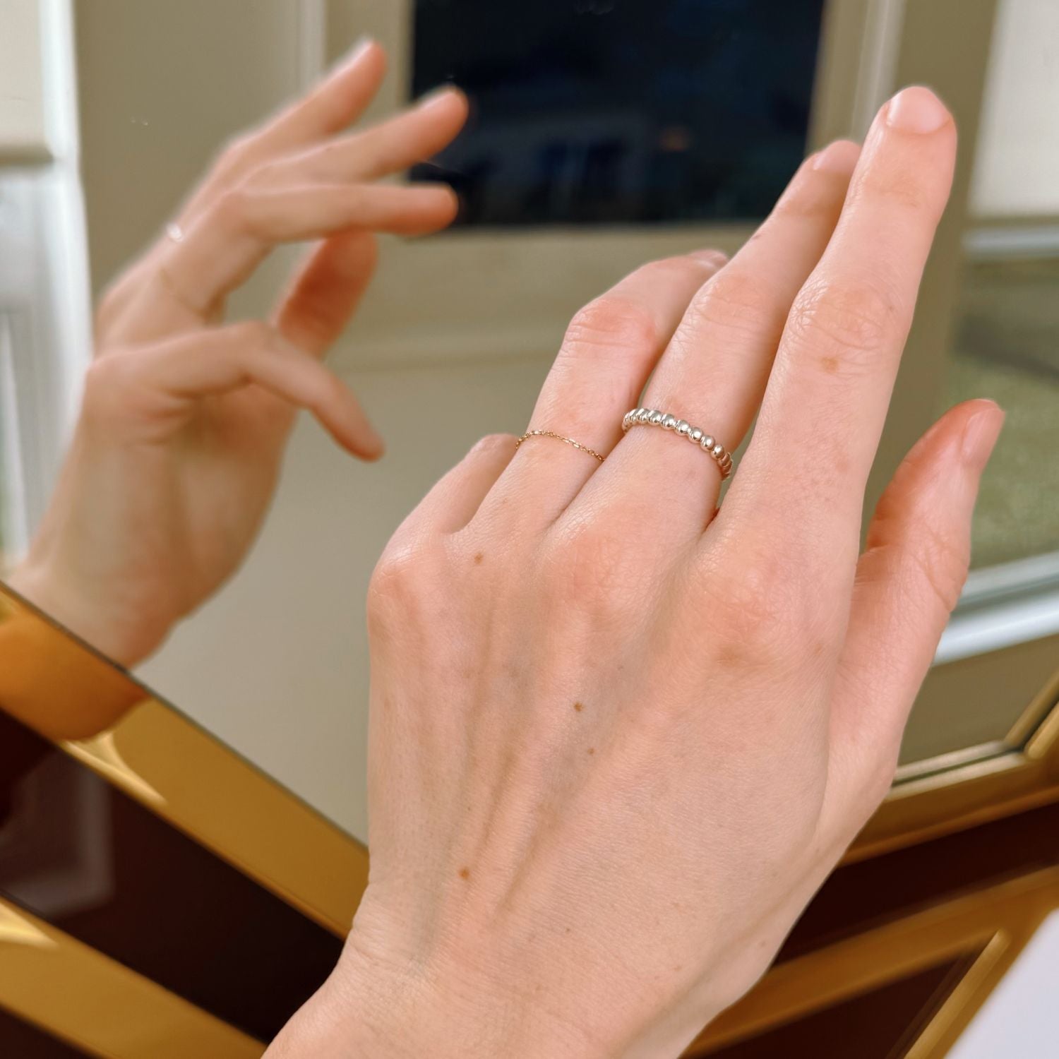 Close-up of hands with a beaded silver ring in front of a mirror