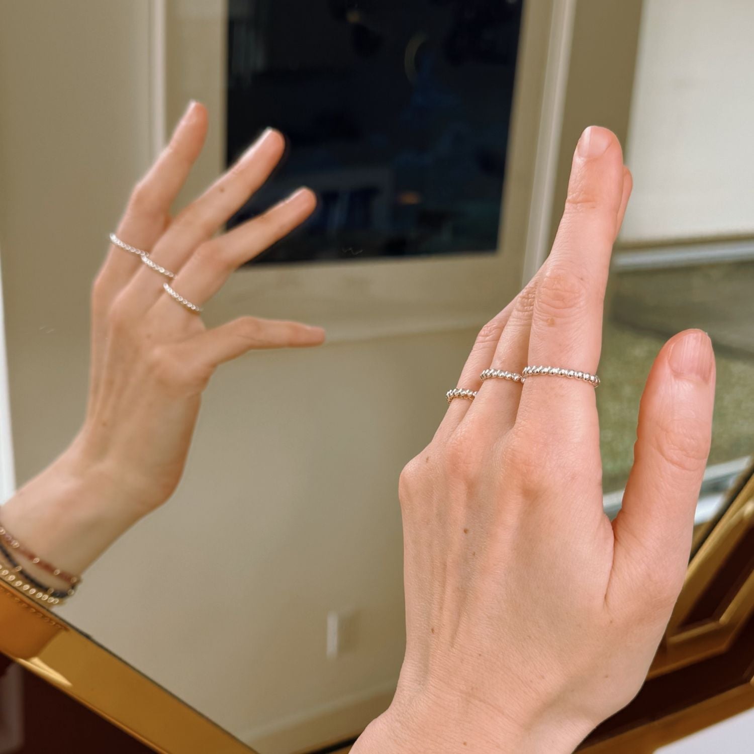 Close-up of hand wearing silver rings with a blurred mirror background
